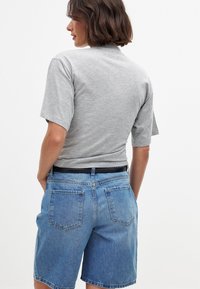 Pelēka īsām piedurknēm T-kreklā, apvienota ar augsto jostasvietu ziliem džinsu šortiem, ar brīvu piegriezumu un aizmugures kabatām. Tīrs un vienkāršs dizains.