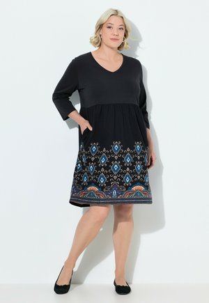 Schwarzes Kleid mit V-Ausschnitt und Dreiviertelärmeln, versehen mit einem gemusterten Saum in Blau, Orange und Creme. Mit Taschen.