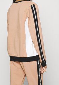 Světle hnědá mikina s černými a bílými panely, kontrastními bočními pruhy, žebrovanými manžetami a klasickým kulatým výstřihem.