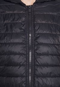 Doudoune noire à fermeture zippée, avec un design matelassé et une capuche. Le matériau semble brillant, avec une texture lisse et des poches intégrées.