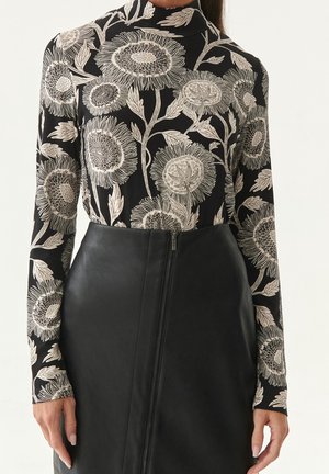 Haut à manches longues noir avec des motifs floraux blancs, associé à une jupe en cuir noir taille haute avec une fermeture éclair sur le côté.
