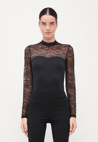 Černý body s krajkovými dlouhými rukávy a vysokým krkem. Korzet je hladký a na ramenou a rukávech má vlnkový krajkový design.