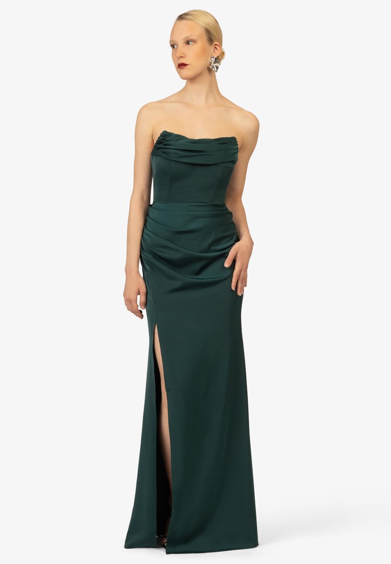 Trägerloses, dunkelgrünes Abendkleid mit drapiertem Oberteil, seitlichem Schlitz und taillierter Passform. Glatte Textur mit schlanker Silhouette und eleganten Details.