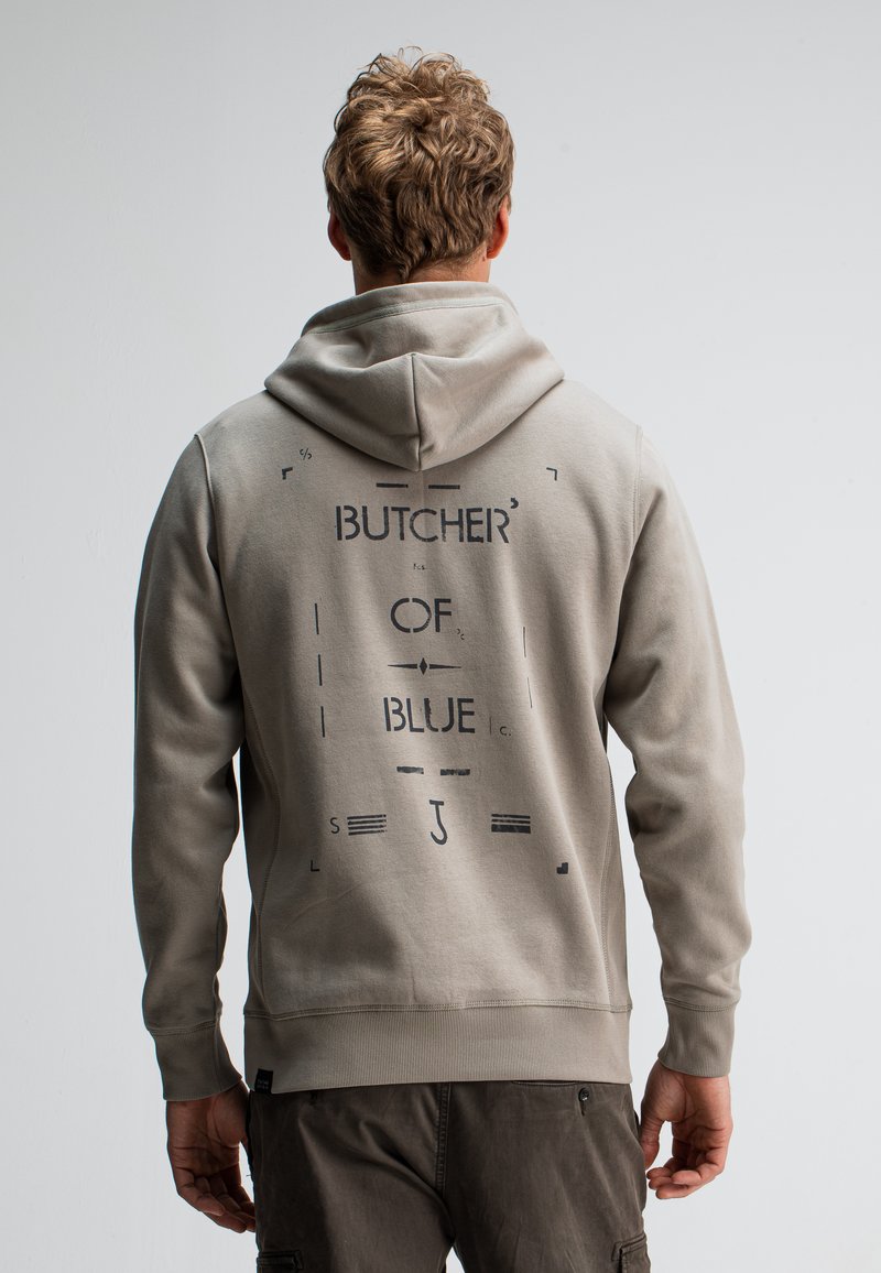 Lichtgrijze hoodie met een zwart grafisch ontwerp waarop "BUTCHER OF BLUE" op de achterkant staat. Het materiaal lijkt zacht, met ribbels aan de mouwen en onderkant.