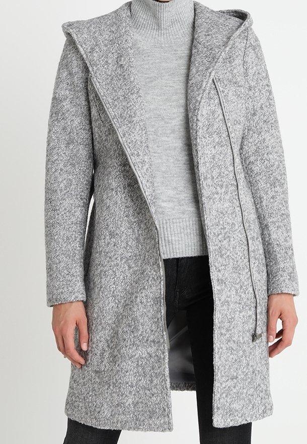 Long manteau gris texturé avec capuche porté sur un pull à col roulé côtelé gris clair et un pantalon noir.