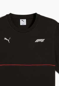 Sort t-shirt med rød vandret streg, med Puma-logoet til venstre og et Formel 1-logo til højre.