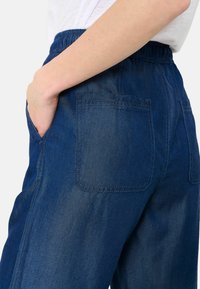 Mörkblå denimbyxor med elastisk midja, sidofickor och två bakfickor. Tyget har en slät yta med subtila blekningseffekter.