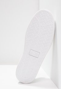 Vit gummisula med texturerat fiskbensmönster och logotyp. Kanten är slät, och botten är något kurvad vid tån.