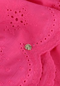 Roze stof met geborduurde bloemenpatronen en kantdetails, met een gouden rozenaccent. Zachte textuur met golvende randen.