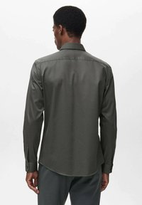Camicia a maniche lunghe di colore verde scuro con una texture liscia, polsini con bottoni e colletto classico, dotata di orlo dritto e sottili dettagli sulle cuciture posteriori.