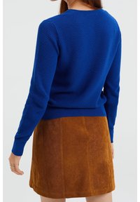 Blå texturerad stickad tröja med rund halsringning och ribbade ärmslut, tillsammans med en brun mocka minikjol.