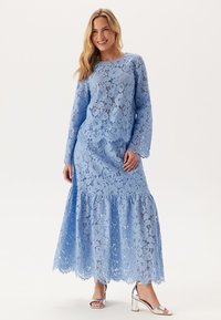 Ljusblå spets maxiklänning med långa ärmar, utsvängd nederkant och blommönster. Inkluderar en rund halsringning och spetsdetaljer. Silverfärgade klacksandaler.