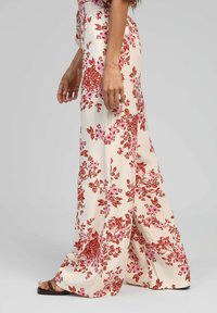 Pantalons larges à fleurs avec une base crème, ornés de motifs de fleurs rouges et roses, en tissu léger et à coupe décontractée.