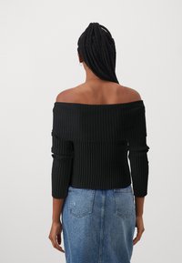 Schwarzer gerippter Pullover mit schulterfreiem Design und langen Ärmeln, mit einem strukturierten Muster. Kombiniert mit einem hellblauen Jeansrock.