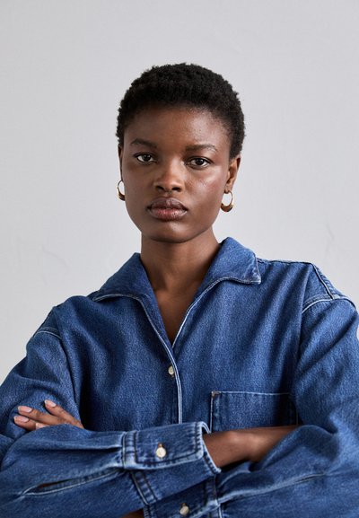 Denim shirt featuring a light blue hue, button closure, and a chest pocket. The fabric is textured and slightly worn.