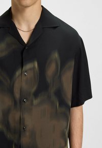 Zwarte korte mouwen shirt met een vervaagd bloemenpatroon in bruintinten, voorzien van een puntige kraag en knoopsluiting aan de voorkant. Glad textile.