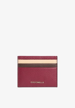 Portafoglio in pelle bordeaux con strisce beige e marrone scuro nella parte superiore, impresso con il logo dorato "COCCINELLE" al centro in basso.