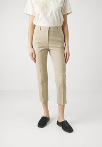 Beżowe spodnie z kordurowej tkaniny z pionowymi paskami, o skróconej długości, wysoki stan, połączone z czarnymi butami typu slip-on. Minimalistyczny design t-shirta.