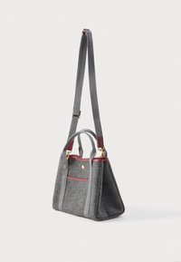 Pelēka rokassoma ar burgundijas apdari, zelta furnitūru, īsām rokturām un garu regulējamu plecu siksnu uz baltā fona.