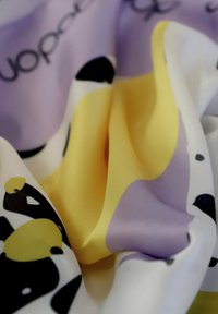 Tejido de seda en varios colores, con grandes formas amarillas, moradas y blancas con acentos en negro. Textura suave y diseño fluido.