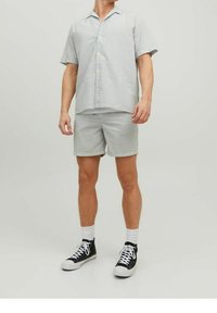 Camisa de manga corta con botones y pantalones cortos a juego en un patrón de cuadros gris claro, combinados con zapatillas negras y calcetines blancos.
