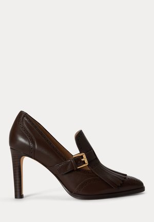 Chaussure à talon haut en cuir marron foncé avec bout pointu, franges décoratives, détails brogue et bride avec boucle dorée.