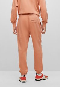Pfirsichfarbene Sweatpants mit elastischen Bündchen, einer Gesäßtasche und einer glatten Textur, kombiniert mit mehrfarbigen Turnschuhen mit Markenlogo.