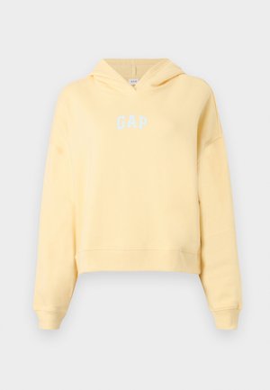 Sweat à capuche court jaune doux avec manches longues et logo "GAP" à l'avant en lettres bleu clair, présenté sur un fond gris uni.