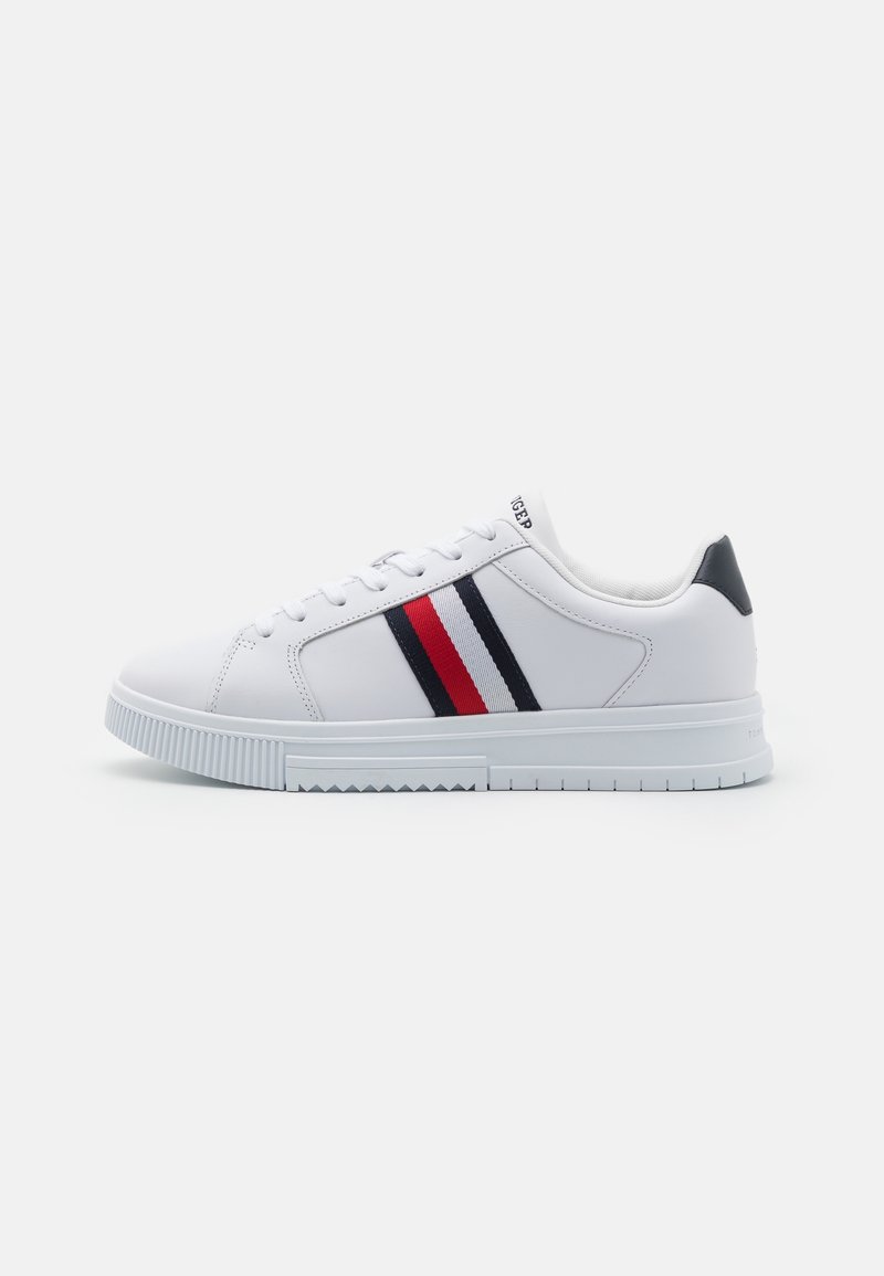 Baskets basses blanches avec des bandes latérales bleu marine, rouge et blanche, des lacets blancs et une languette de talon noire sur fond blanc.
