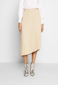 Falda midi plisada beige con cintura elástica, que presenta pliegues pronunciados y un dobladillo asimétrico, combinada con botines de tobillo de textura en estampado de serpiente.