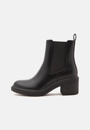 Bottine en cuir noir avec panneau latéral élastique, languette au talon et talon bloc sur fond clair.