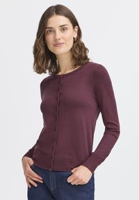 Burgunderfarbener Cardigan mit rundem Ausschnitt, langen Ärmeln und einer vorderen Knopfleiste. Rippstrick-Details an den Bündchen und dem Saum. Weiche Textur.