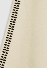 Béžová tkanina s výrazným černým stehem podél okraje, s texturovaným povrchem a viditelným tkaným vzorem.