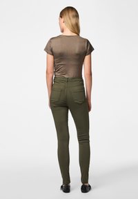 Brown fitted t-shirt with short sleeves paired with high-waisted olive green skinny jeans. Smooth texture, three back pockets, and black flats.