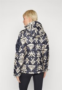 Casaco puffer acolchoado com exterior azul marinho, apresentando padrões abstratos em creme. Inclui capuz e punhos elásticos para um ajuste confortável.