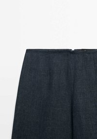 Mörka denimbyxor har en rak skärning med en slät textur och en dragkedja i midjan. Två framfickor är synliga.