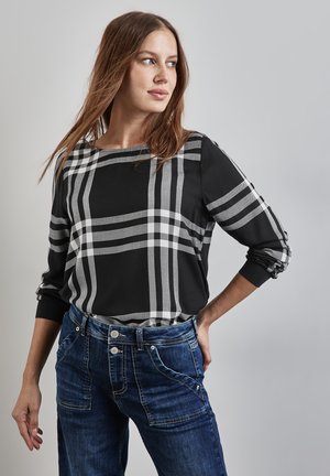 Top a scacchi nero e grigio con maniche a tre quarti, realizzato in tessuto morbido. Abbinato a jeans in denim blu con tasche e cerniera.