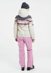 Giacca di corduroy bianca con un motivo a zig zag colorato sul retro, abbinata a pantaloni rosa e stivali da sci neri, dotata di cappuccio e polsini a coste.