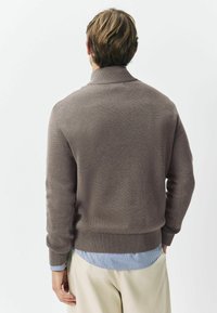 Brązowy sweter dzianinowy z prążkowanym kołnierzem i mankietami. Nosi się go na jasnoniebieskiej koszuli w paski, zestawiony z beżowymi spodniami.