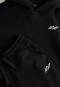Ensemble sweat à capuche noir et pantalon de jogging en tissu doux. Présente un col côtelé, une taille élastique et un logo blanc sur les deux pièces.