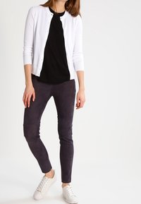 Bílý kardigan, černá košile, tmavě šedé slim kalhoty a bílé tenisky. Kardigan má design s knoflíky; kalhoty mají hladkou texturu.