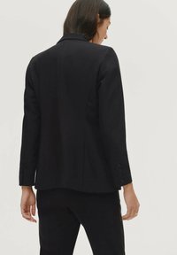Zwarte blazer met een gestructureerd ontwerp, enkele knoopsluiting en manchetten met drie knopen. Gladde stof met een op maat gemaakte pasvorm en een ventilerende achterkant.