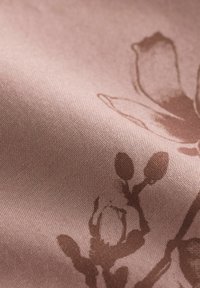 Tekstil s mekim, ružičastim materijalom s suptilnim cvjetnim uzorkom u smeđoj boji, ističe glatku teksturu i delikatan dizajn.