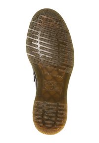 Semelle en caoutchouc noir avec adhérence texturée, présentant des rainures horizontales et verticales, ponctuées de motifs circulaires pour la traction.