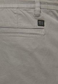 Lichtgrijze katoenbroeken met een gladde textuur, voorzien van een achterzak en een klein zwart logo patch. Aangeklede tailleband detail.