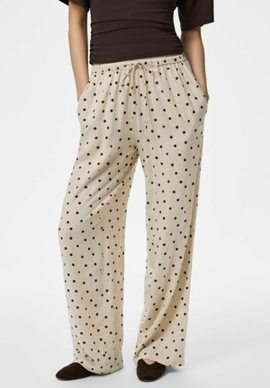Pantalon beige à jambes larges avec des pois marron, taille élastique avec cordon, porté avec des chaussures noires et un haut foncé.