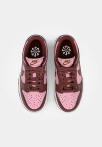 Sapatilhas Nike com um upper em pele rosa e castanho, apresentando biqueira perfurada, atacadores castanhos e sola em borracha branca. Logotipo na lingueta.