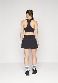Svart racerback sportstop och utsvängd kjol, båda i ett slätt tyg. Outfitten kompletteras med vita strumpor med blå ränder och svarta skor.