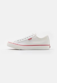 Sneaker bianco in tela con dettagli rossi, punta rotonda, design con lacci, suola in gomma e una piccola etichetta con logo vicino al tallone. Texture liscia.