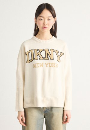 Kremfarget genser med strikkedesign, brede ribbestrikkede mansjetter og grafisk "DKNY NEW YORK" i mørk og lys brun skrift.